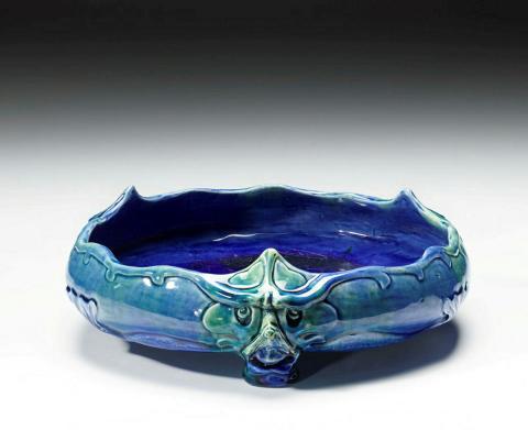 Artwork Fruit bowl this artwork made of Earthenware, hand built with low in-curving sides modelled with three grotesque masks which terminate in a foot.  Glazed green and blue, created in 1931-01-01