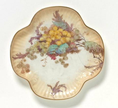 Artwork Plate this artwork made of Porcelain (parian) transfer printed in brown and hand coloured in yellow, green and mauve with a design of wattle, created in 1884-01-01