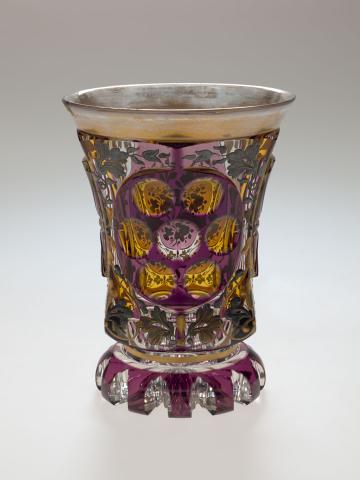 Artwork Beaker this artwork made of Glass, cased amethyst over clear and cut away in panels stained yellow.  Applied with gilt and gunmetal floral motifs, created in 1840-01-01
