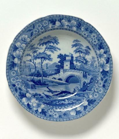 Artwork Soup plate this artwork made of Stoneware (stone china) transfer printed in blue within a landscape showing a tower, bridge and cottage.  Floral border, created in 1815-01-01