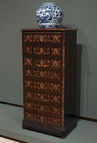 Artwork Wellington chest this artwork made of Ebonised wood, the eight drawers inlaid in various woods with scrolls, flowers and cartouches framing the bronze key escutcheons and lion mask handles. Brown marble top