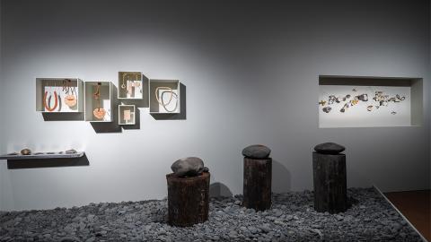 An installation view of a collection of works: some framed on the wall; some raised as pillars on the ground, some set into shelves.