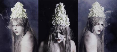 A triptych of photographs featuring a person wearing white face and body paint, red lipstick, and a conical hat made of flowers.