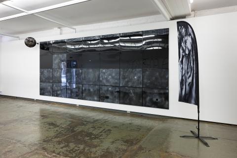 An installation view of a gallery space with a series of black screens on a white wall, with a polished concrete floor below.