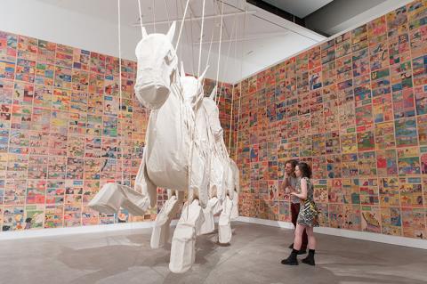 An installation view of a larger-than-life-size sculpture of three made of linen, suspended from the ceiling.