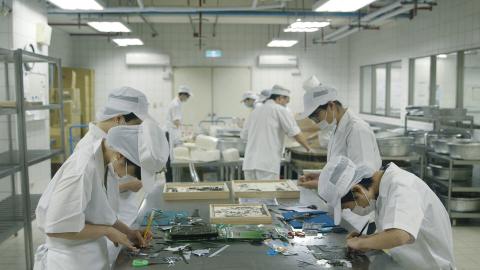 A photograph of people in a lab-like environment at work wearing white protective clothing.