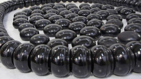 An installation view of a sculptural work made from smooth, shiny black bowls arranged in cirlces.