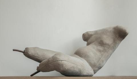 A figure rendered in cement, missing a head, arms and feet, positioned as if about to lie down or stand up.
