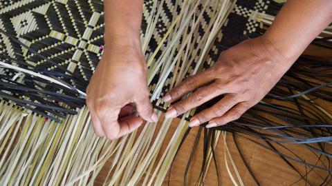 A photograph of a pair of hands weaving flax.