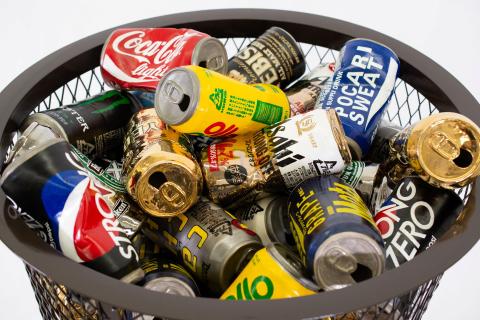 A close-up photograph of many colourful, crushed soda cans in an iron trashcan. (These realistic cans are in fact ceramic, made by Kimiyo Mishima.)