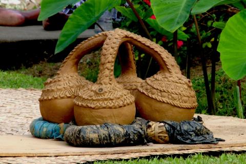 A clay water vessel with four lobes sits on a mat in a garden.