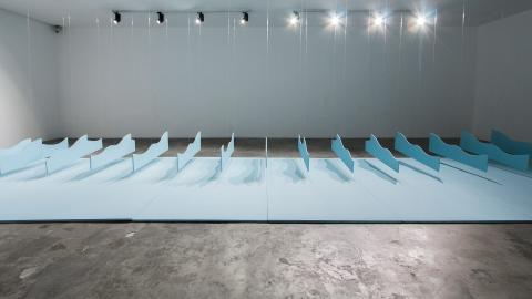 An installation view of a kinetic work with many sculptural 'waves' rising over a blue floor.