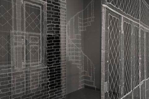 Architectural features like windows and stairs woven into lace tableaux, suspended in a gallery.
