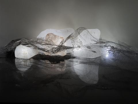 A sculptural work with 'stones' giving off a warm white glow, draped in nets and reflective material.