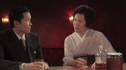 A still photograph from a video work in which the artist portrays both a man and a woman, who sit at a bar together, looking at each other.