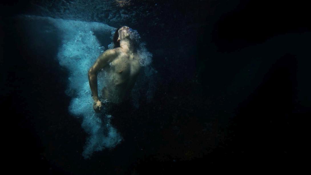 A still photograph of a masculine-appearing person making a splash in dark, almost black water (DETAIL)