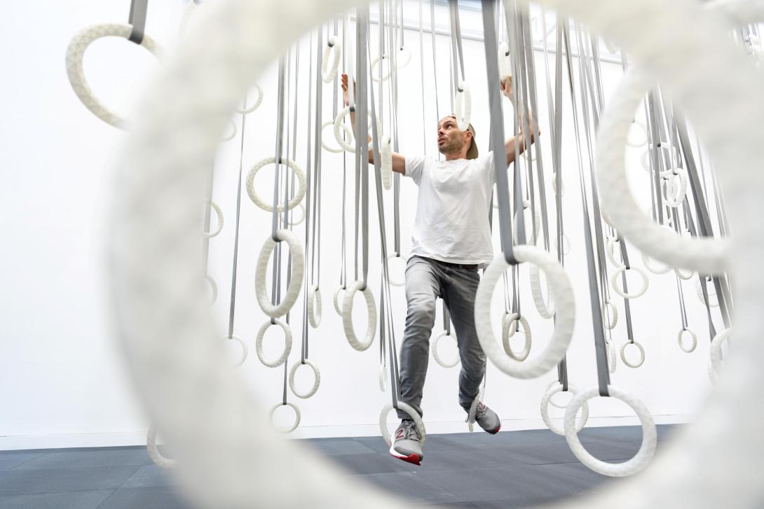An installation view of a large-scale artwork made of white hoops suspended from above, which visitors can use to climb across the gallery space.