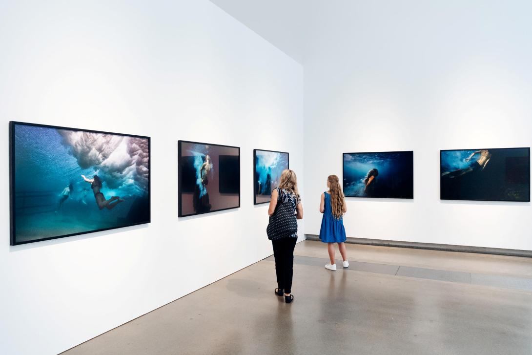 An installation view of five underwater photographs by Paul Blackmore hung on white walls in a bright gallery space.
