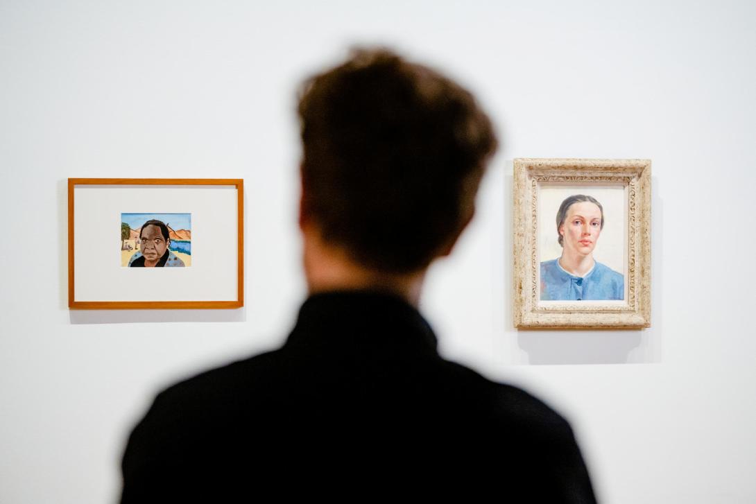 An installation view taken from behind a visitor's head; the visitor looks upon two small self-portrait works hung on a white gallery wall.