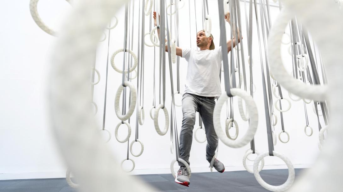 An installation view of a gallery visitor climbing across a series of white hoops suspended from the ceiling for an interactive artwork.