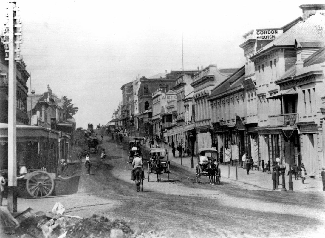 A black-and-white photograph of a streetscape in which people can be seen riding horses and small