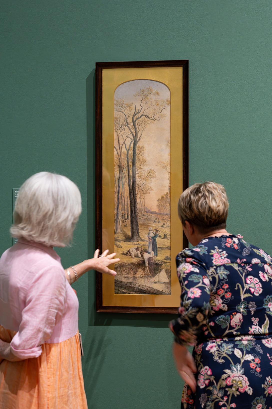 An installation view of a long, narrow, portrait-oriented oil painting installed on a sage-green wall, with two visitors looking on, pointing at details.