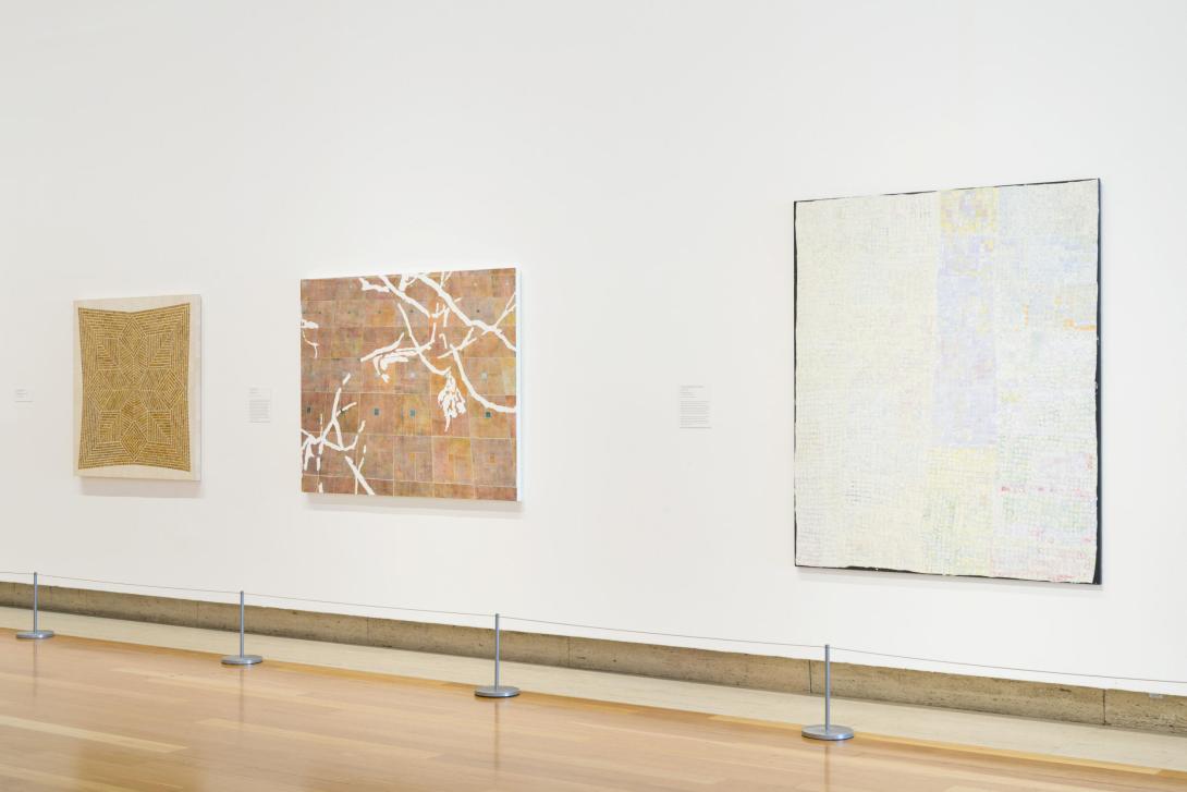 An installation view, with three earth-toned paintings hung on a white gallery wall.