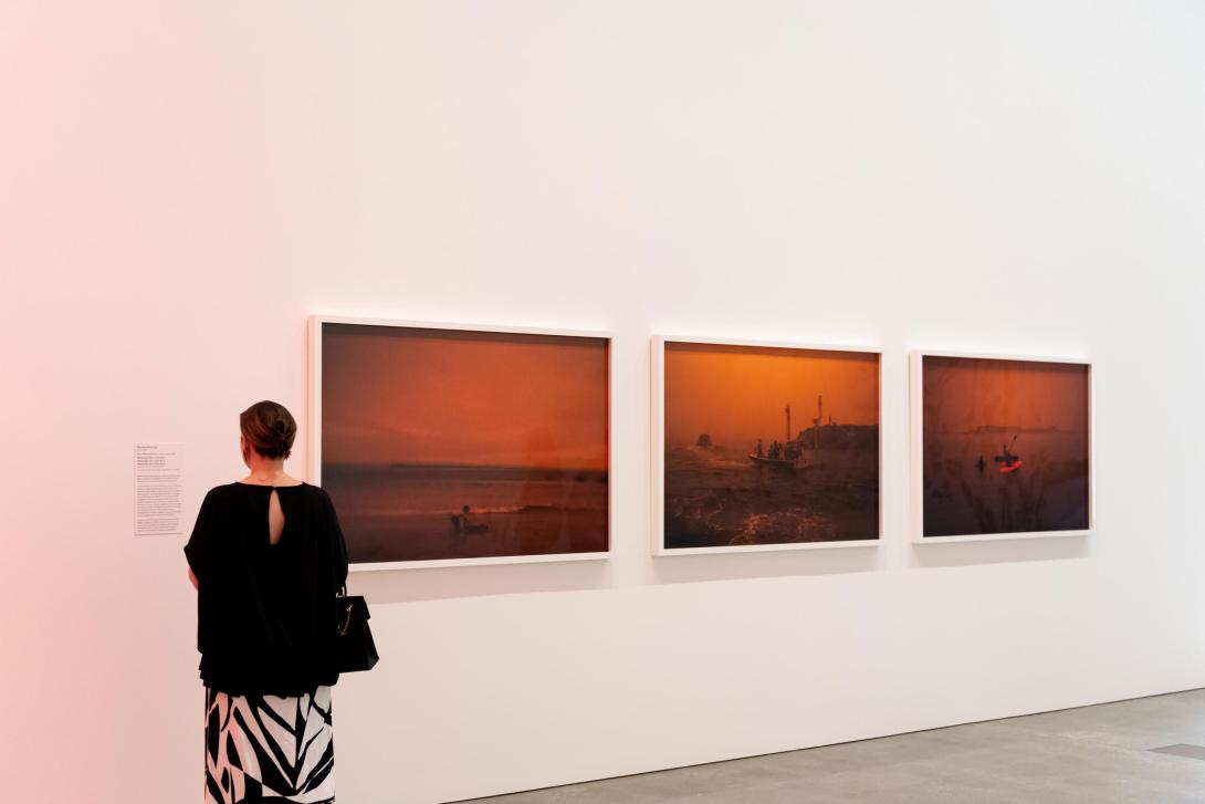 An installation view of a gallery space, with three photographs of landscapes photographed with red post-bushfire skies