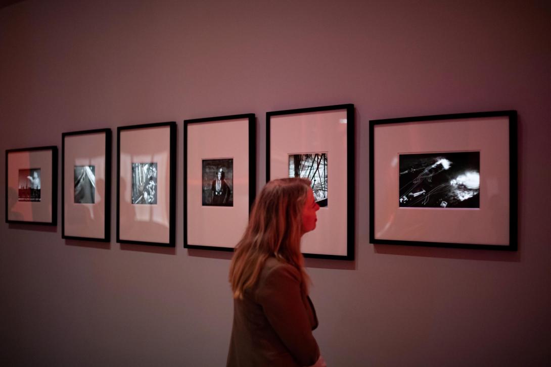 An installation view of six photographs on a gallery wall, with a visitor looking on.
