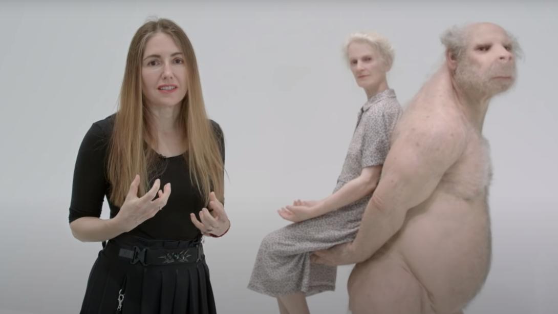 An artist stands before a sculpture of a nude creature carrying an elderly lady on its back.