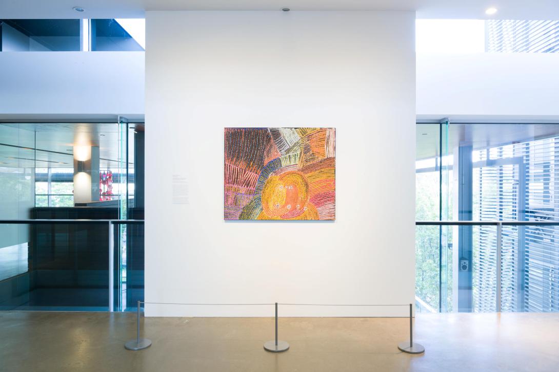 A colourful painting installed on a gallery wall, with windows either side.