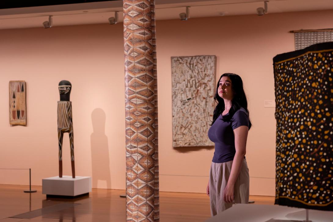 Works of Indigenous Australian art installed in a gallery space, with a visitor looking on.