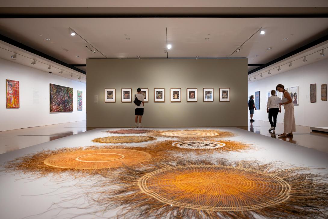 An installation view of a gallery space, with woven mats in the immediate foreground of the photo.