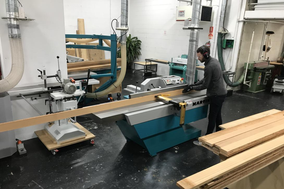 A photo of a man in a studio using a large machine to construct a timber painting-stretcher