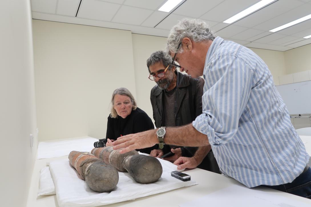 Researchers stand around two sculptures in a white-walled museum conservation space.