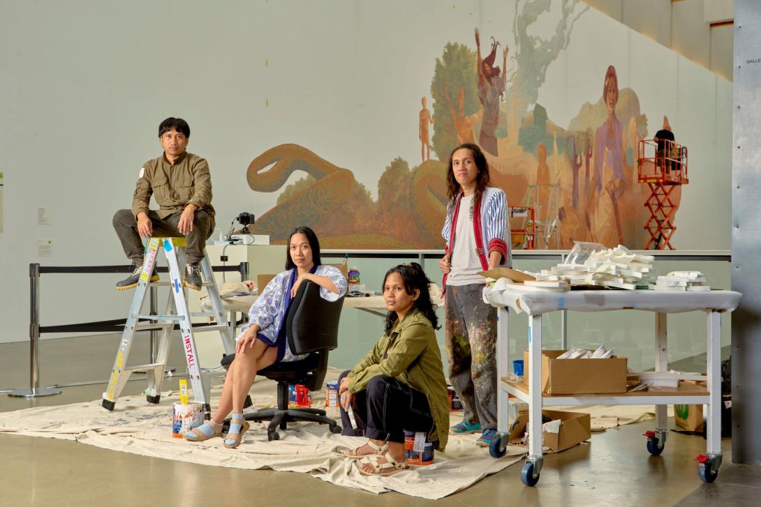 Four artists pose in front of a large-scale mural they have painted on a white gallery wall 