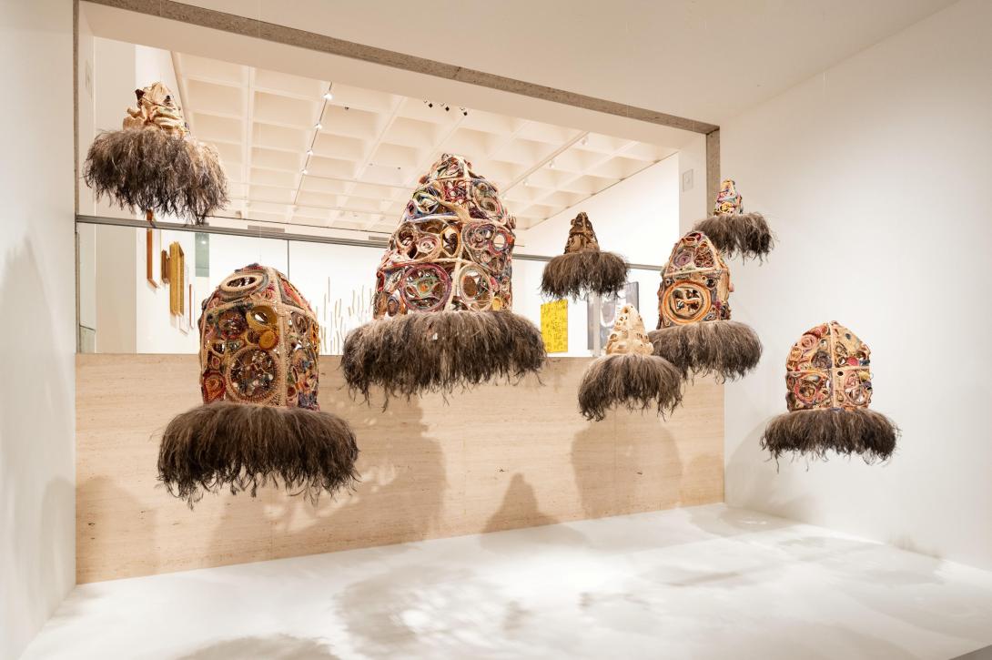 An installation view of eight woven sculptures suspended together in a gallery space.