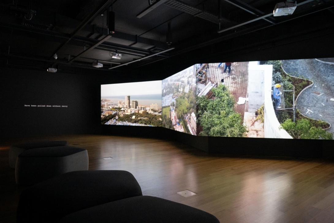 An installation view of a multi-screen video installation in a dimmed gallery space