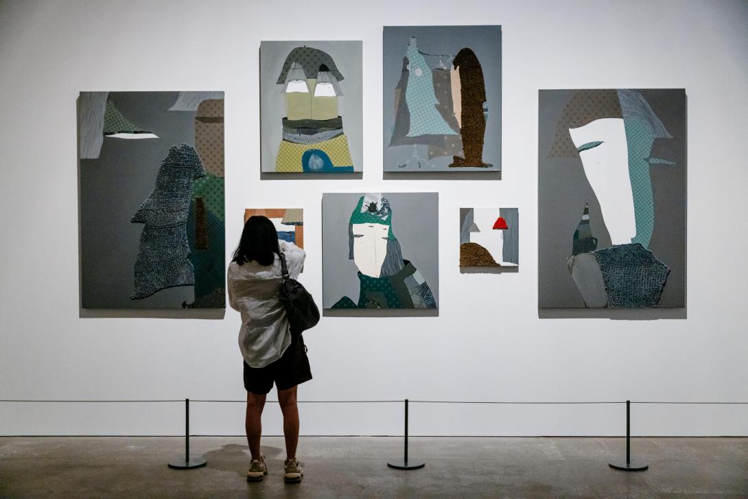 Paintings installed on a white wall in a gallery space, with a person looking on