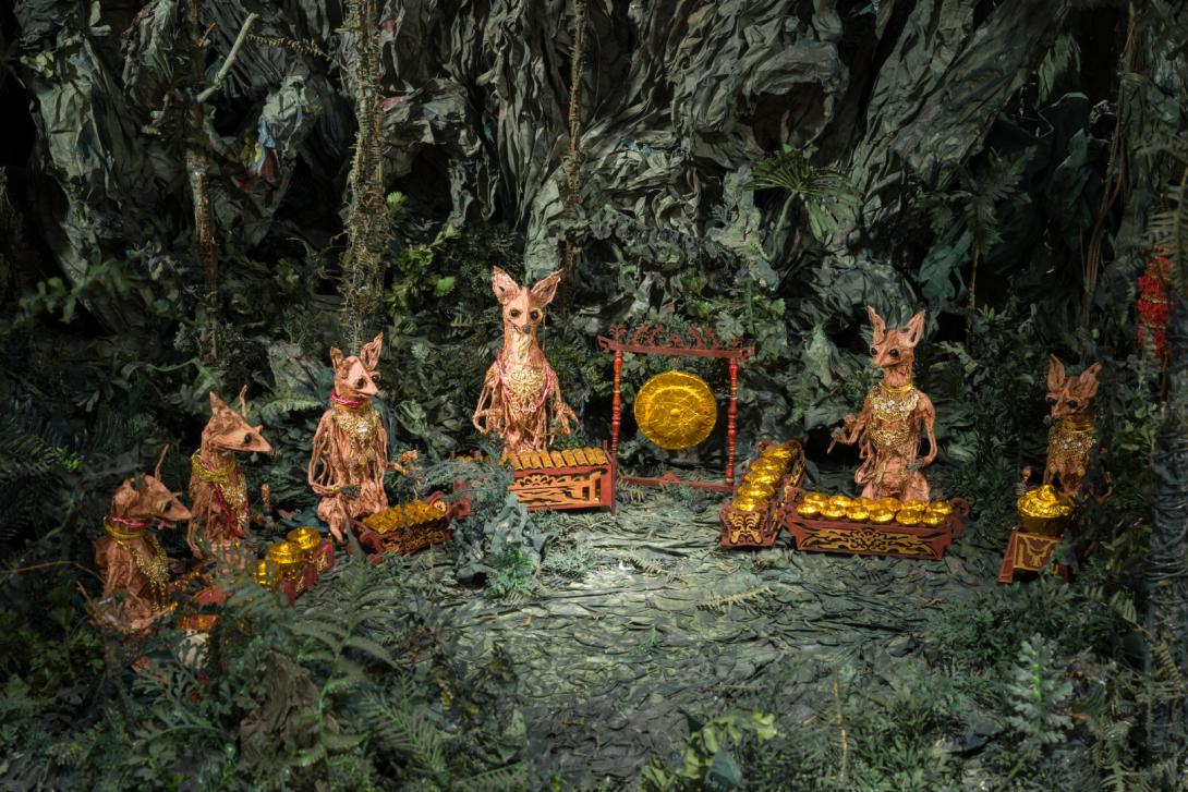 A close-up photograph capturing a detail of a sculptural work made from paper, depicting tiny animals playing musical instruments in a forest