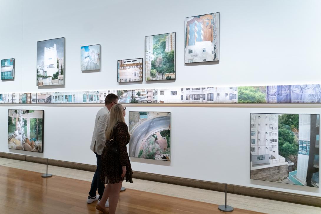 Oil paintings of scenes in Hong Kong installed salon-style on a white gallery wall