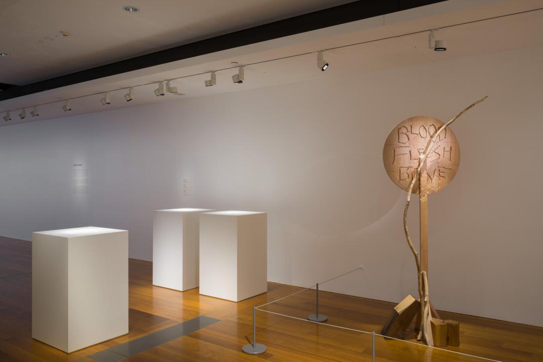 Works on paper installed flat on plinths in a gallery space, alongside a tall, engraved wood assemblage