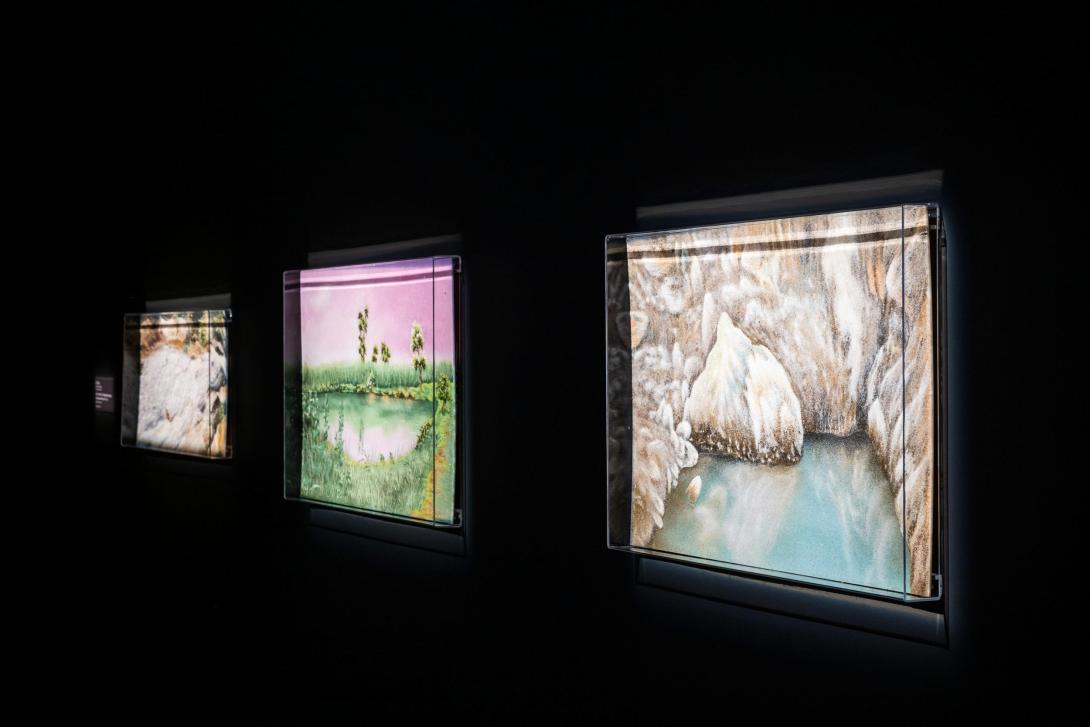 Colourful artworks lit from behind, installed on a dark gallery wall