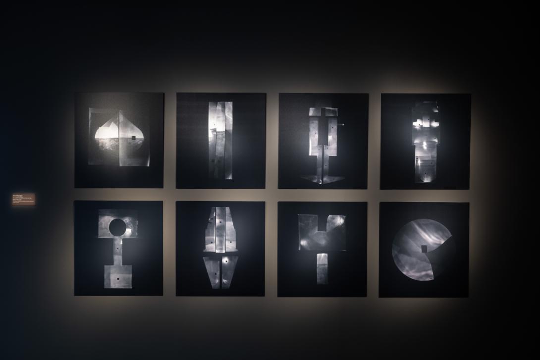 Eight dark-toned photographs installed on a dark gallery wall