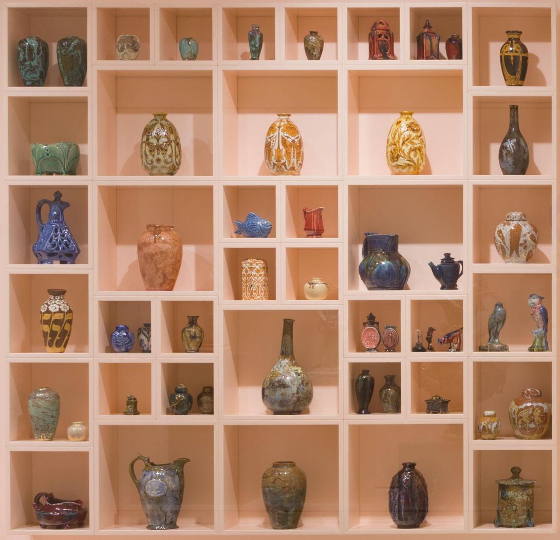 A photograph of a salmon-pink, square display cabinet, displaying many colourful miniature ceramics.