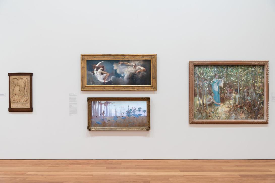 A photograph of four paintings installed on a white wall in a gallery with warm-toned polished wooden floors.