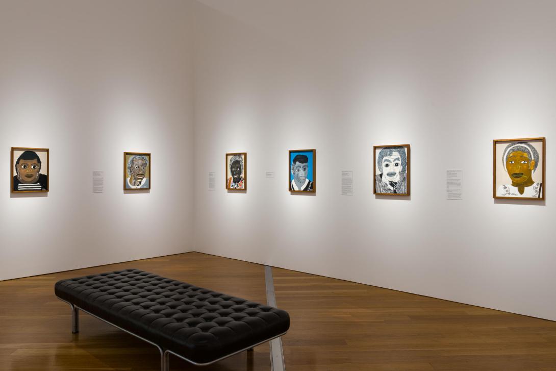 Six portraits by Heather Marie (Wunjarra) Koowootha, installed across two walls in a gallery space, with a bench in the foreground