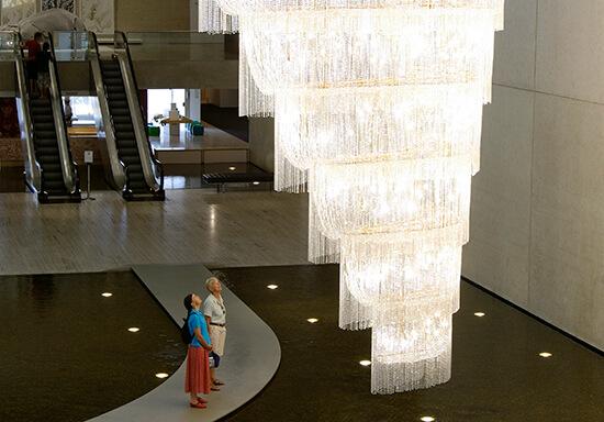 Two people in the Gallery's water mall look up at a huge, elaborate chandelier.
