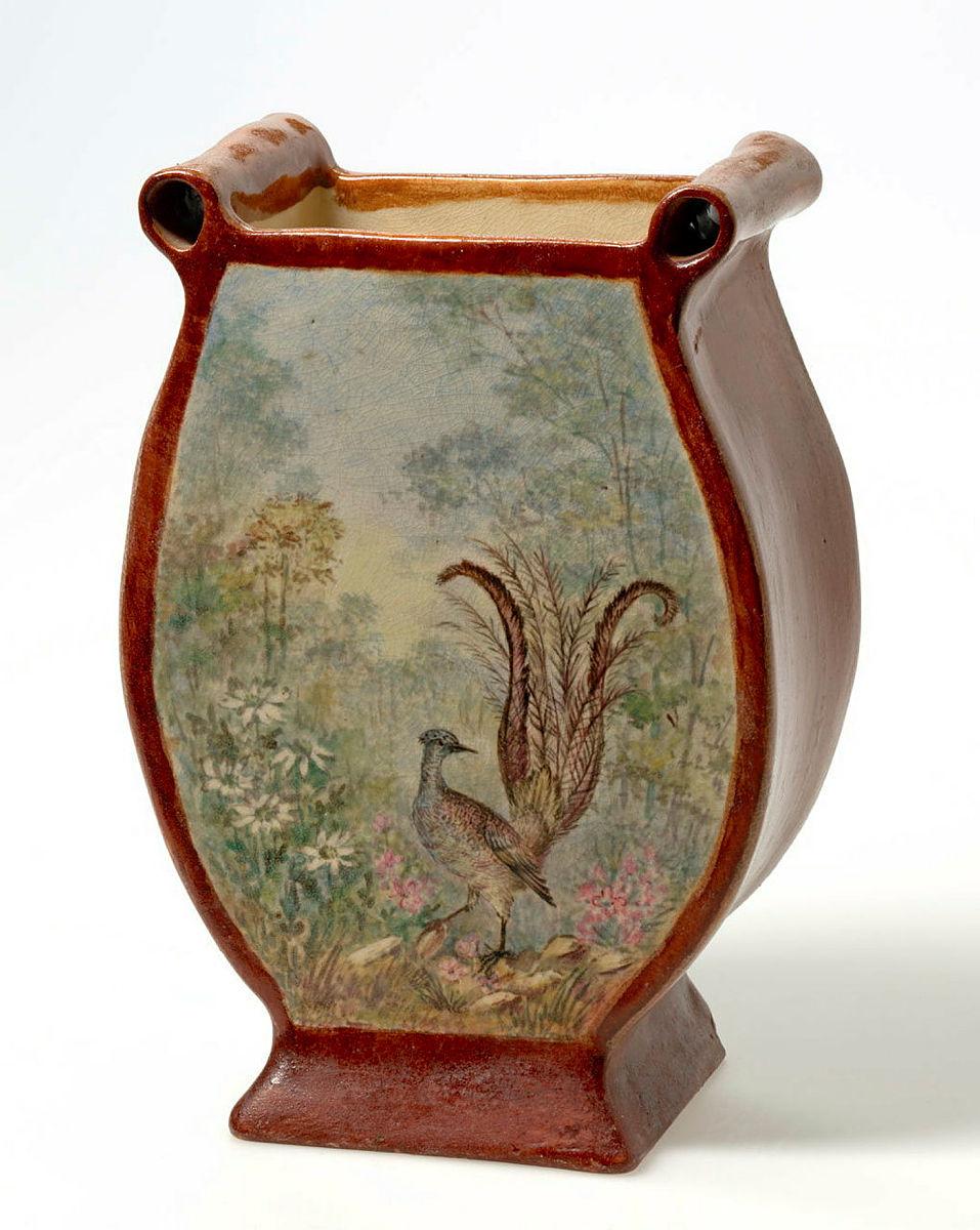 Artwork Lyre-bird vase this artwork made of Earthenware, slab and hand built in the shape of a lyre with rust red glaze and painted on two sides with lyrebirds in bushland settings in polychrome underglaze, created in 1934-01-01
