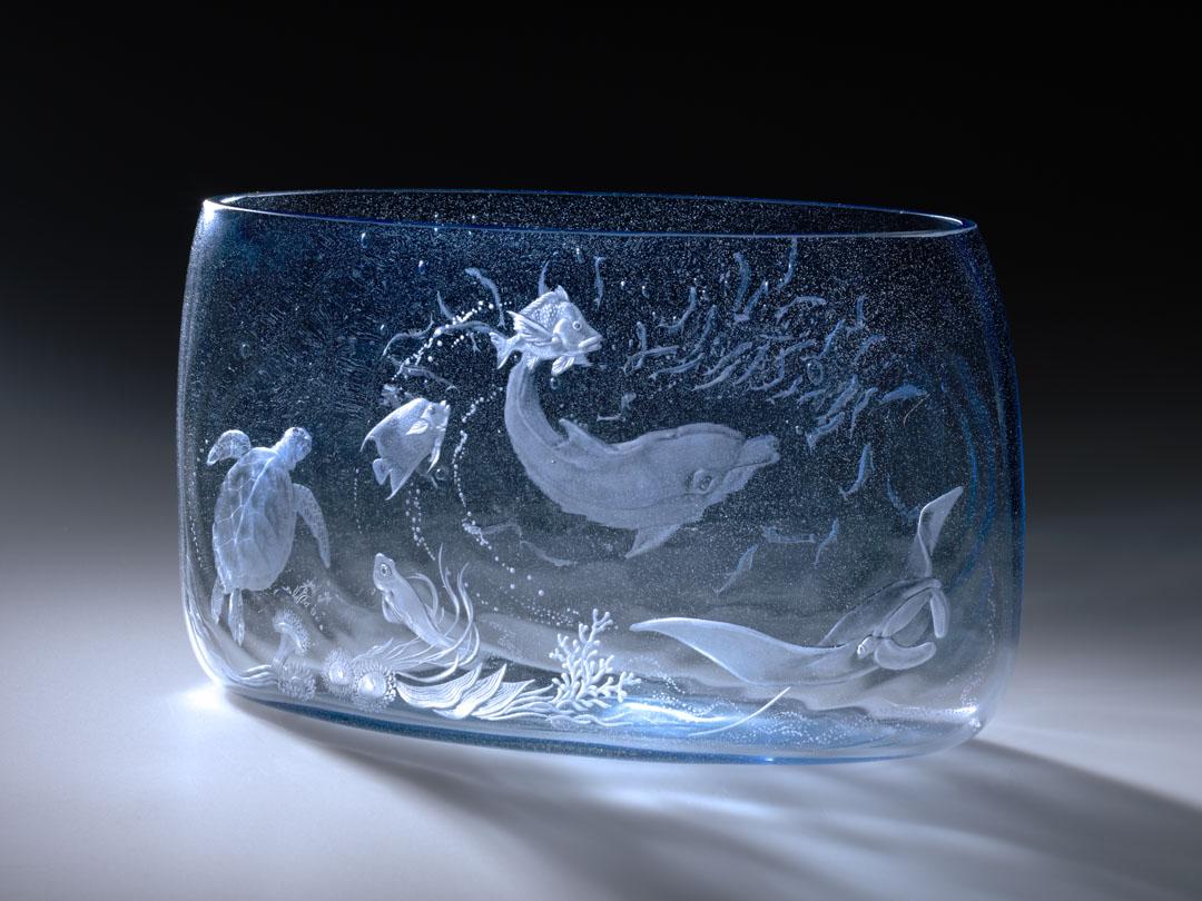 Artwork Vase:  The Barrier Reef this artwork made of Hot blown light blue rippled glass engraved with a dolphin, manta ray, fish and coral, created in 1983-01-01
